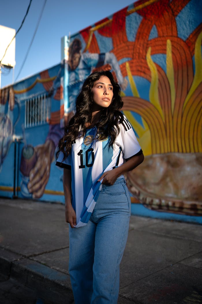 Mastering the First Impression: Your intriguing post title goes here Young woman in Argentina football jersey poses by colorful street mural.