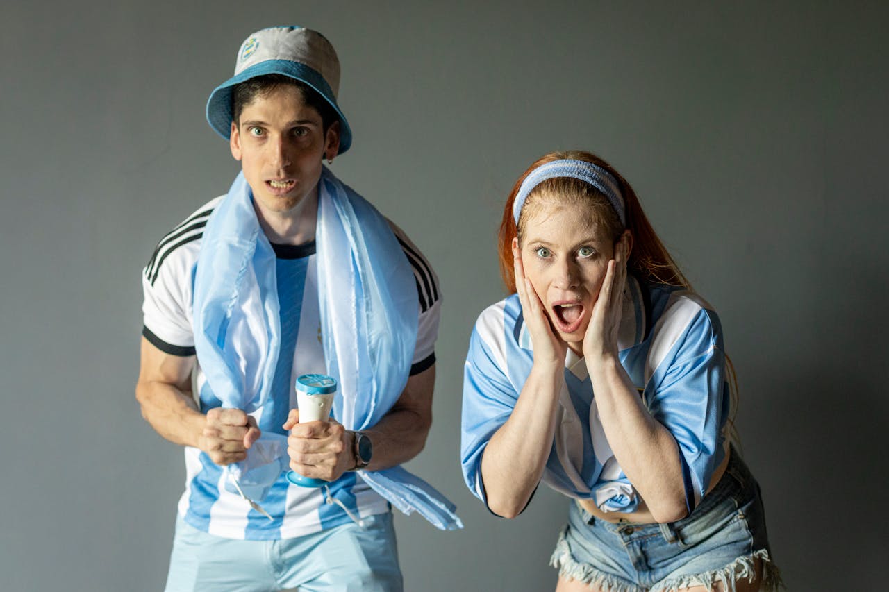 services-03 Two passionate Argentine fans celebrating with excitement, wearing team colors indoors.