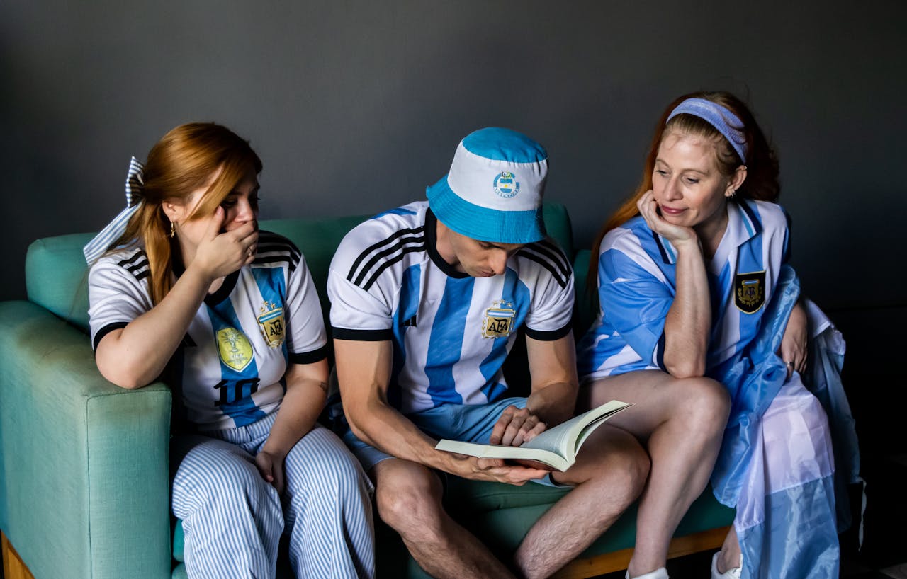 services-02 Three soccer fans in Argentina jerseys reading a book indoors